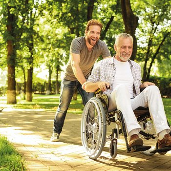 Junger Mann schiebt älteren Herrn im Rollstuhl